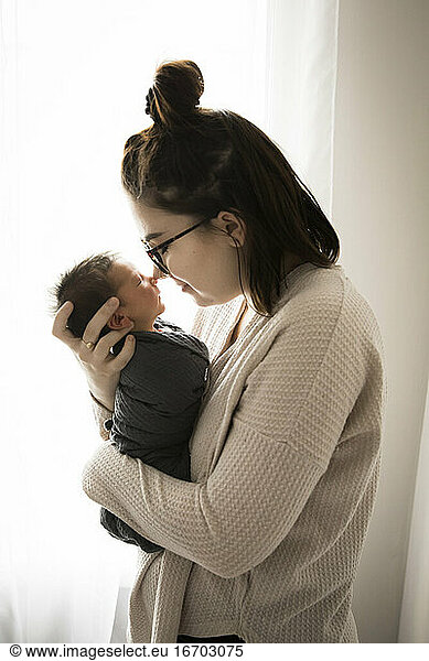 Beleuchteter Hipster Millennial Mom Nose to Nose mit Swaddled Newborn Sohn