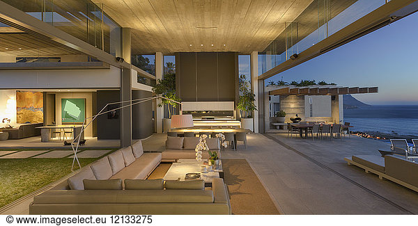Beleuchtetes modernes Luxus-Wohnhaus: Wohnzimmer mit Zugang zur Terrasse in der Abenddämmerung