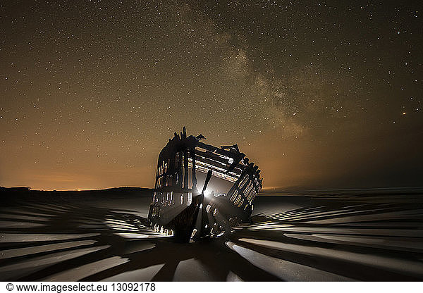 Beleuchtetes Peter-Iredale-Schiff auf Sand gegen den nächtlichen Sternenhimmel