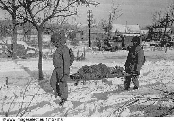 BELGIEN Malmedy -- 17. Dezember 1944 -- Der Leichnam eines amerikanischen Soldaten wird auf einer Bahre aus dem Gelände in der Nähe von Malmedy  Belgien  getragen  wo die Deutschen am oder um den 17. Dezember 1944 zahlreiche Gräueltaten begingen. Der deutsche Gegenangriff  der später als Ardennenoffensive bekannt wurde -- Bild von Taylor / Lightroom Photos / US Army *Beste verfügbare Qualität. Nicht auf Staub oder Kratzer retuschiert.
