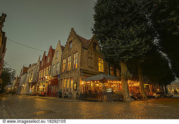 Belgium  West Flanders  Bruges  Cobblestone street stretching in front of sidewalk cafe and row of town houses at dusk