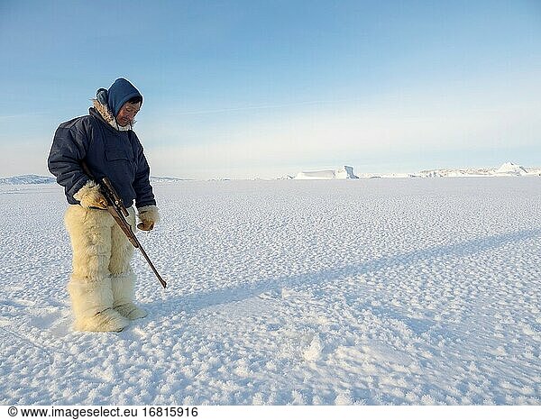 Beobachtung eines Atemlochs einer Robbe. Inuit-Jäger in traditionellen Hosen und Stiefeln aus Eisbärenfell auf dem Meereis der Melville-Bucht bei Kullorsuaq in Nordgrönland. Nordamerika  dänisches Territorium.