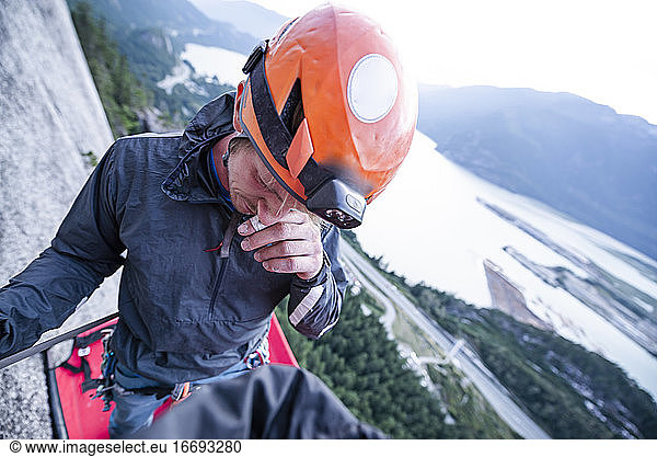 Bergsteiger mit Helm  der sich an der Nase kratzt  steht auf dem Portaledge bei Sonnenuntergang