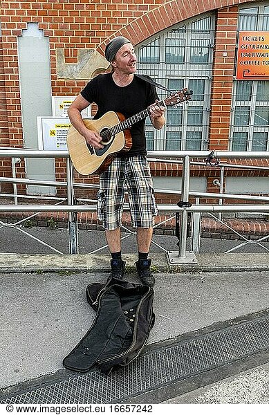Berlin  Deutschland. Junger Erwachsener  männlich  kaukasisch  spielt seine Gitarre auf der Straße an einem U/S-Bahnhof.