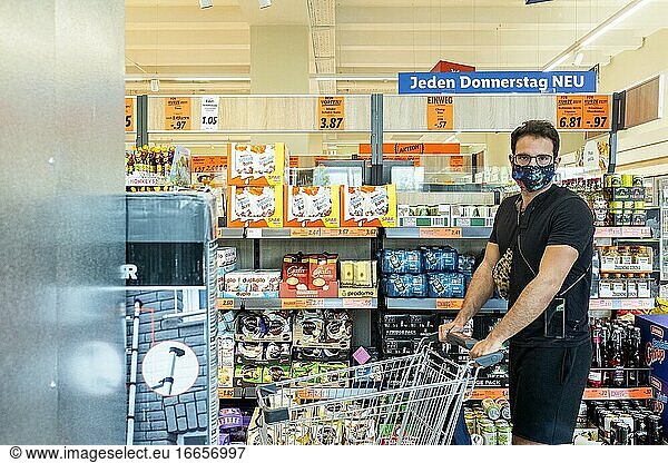 Berlin  Deutschland. Älterer schwuler Mann  der in einem örtlichen Supermarkt Lebensmittel einkauft und aufgrund des Corona-Ausbruchs und der Covid-19-Krise einen schützenden Mundschutz trägt. In Deutschland ist das Tragen von Gesichtsmasken in allen geschlossenen  öffentlichen Räumen Pflicht.