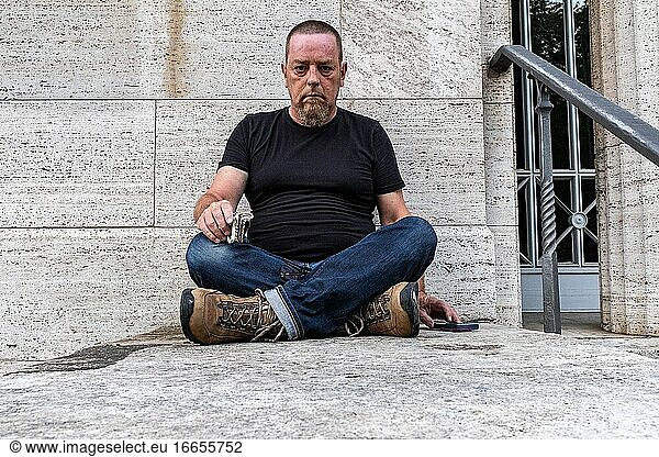 Berlin  Deutschland  Porträt eines erwachsenen  kaukasischen Mannes  der vor einer grauen Wand sitzt.
