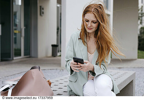 Berufstätige Frau benutzt Smartphone auf einer Bank