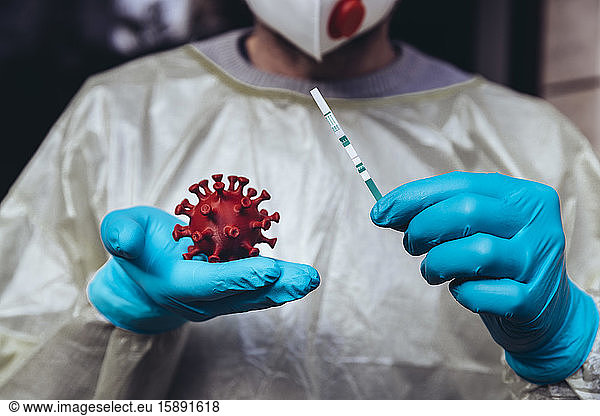 Beschäftigte im Gesundheitswesen halten ein Modell des Coronavirus und einen Lateral-Flow-Test