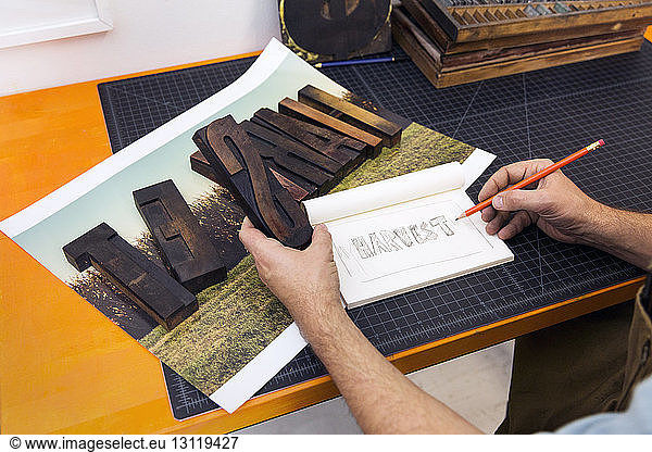 Beschnittenes Bild eines Mannes  der hölzerne Alphabete hält und in Papier kopiert