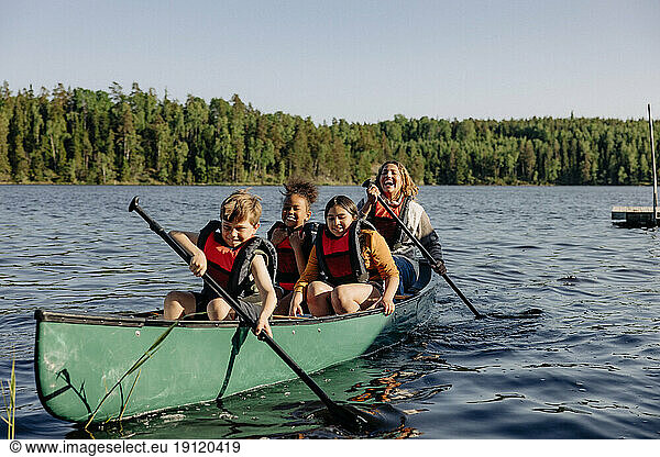 Betreuer und Kinder paddeln auf dem See gegen den Himmel im Sommercamp