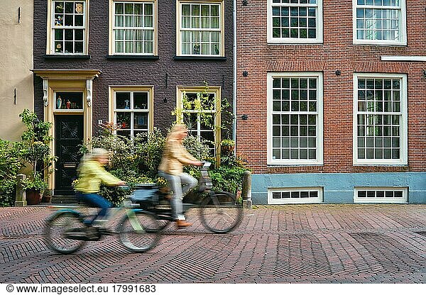 Bewegung verschwommen Fahrradfahrer Radfahrer Frau und Kind auf dem Fahrrad sehr beliebtes Transportmittel in den Niederlanden in Straße mit alten Häusern von Delft  Niederlande  Europa