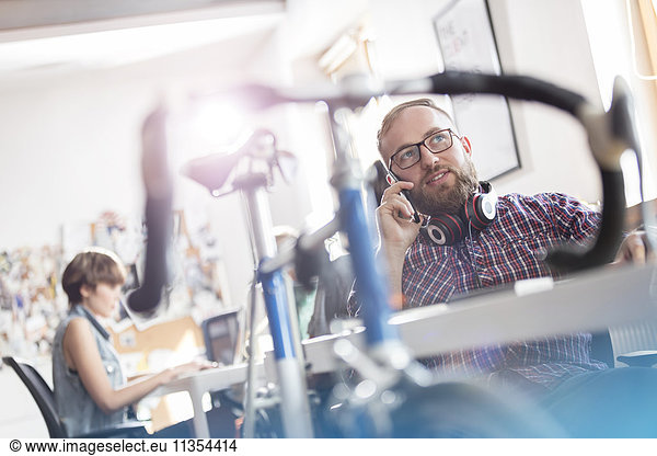 Bicycle leaning against desk next to male design professional talking on cell phone in office