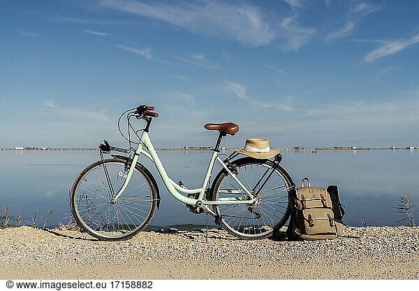 Bicycle parked with backpack leaning on rear wheel with hat on sunny day at Ebro's Delta. Spain