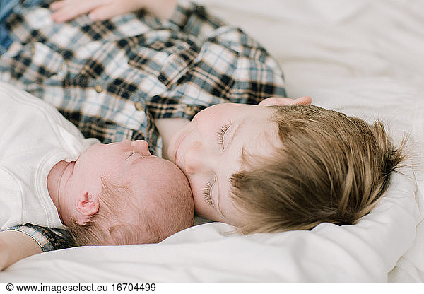 Big brother and newborn baby sister snuggling on bed