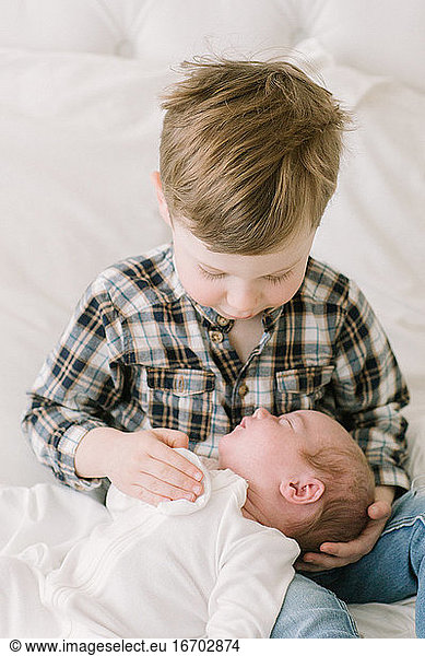 Big brother hold baby sister for first time on bed