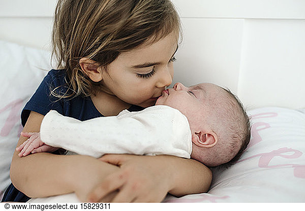Big sister cuddling and kissing newborn sibling