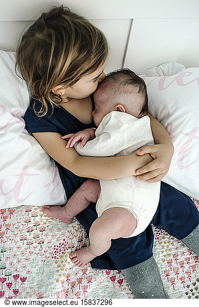 Big sister cuddling newborn baby with bare legs