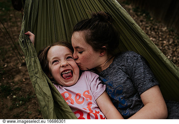 Big sister kissing little sister in hammock outside
