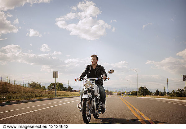 Biker riding motorcycle on road against cloudy sky