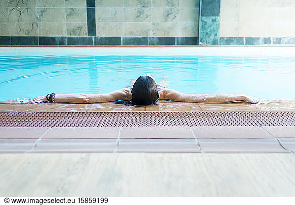 Bikini woman lying relaxing in spa pool on the edge of pool enjoying the blue water