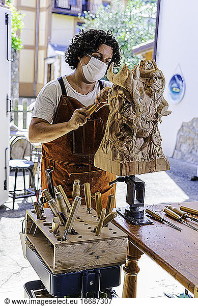 Bildhauerin mit Maske schnitzt Holzfigur