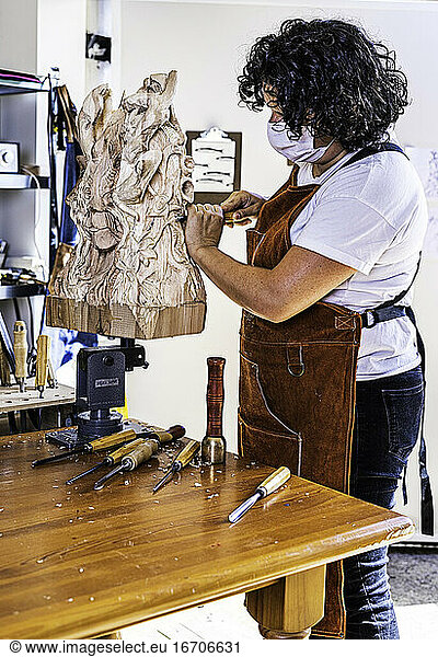 Bildhauerin mit Maske schnitzt Holzfigur