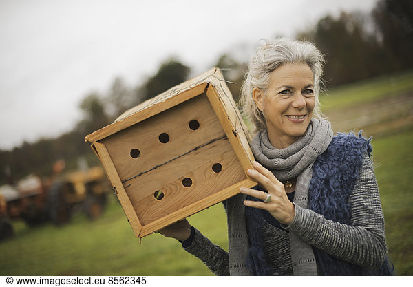 Biolandwirt bei der Arbeit. Eine Frau hält eine Käferbox  eine Holzkiste mit Löchern  in der Insekten nisten können.