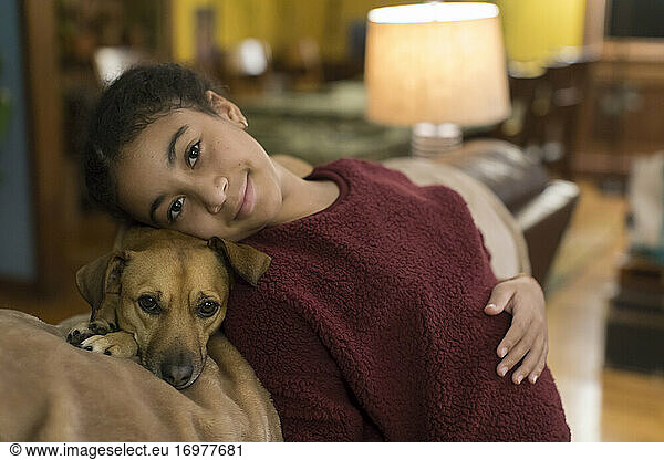 Biracial tween looking at camera while leaning against small brown dog