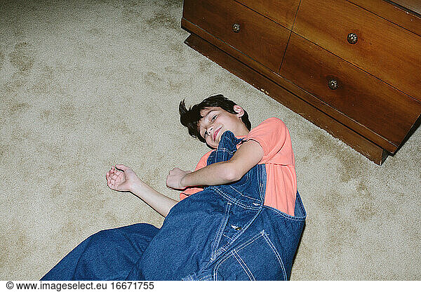 Birdseye view of a boy in oversized overalls lying down on the carpet