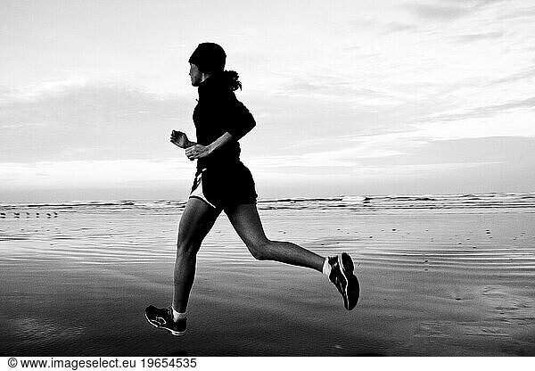 Black and white image of a woman running on a beach.