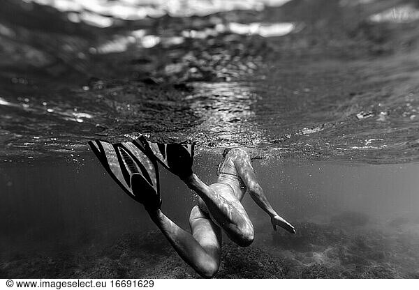 Black and white photo of female swimming with fins in ocean