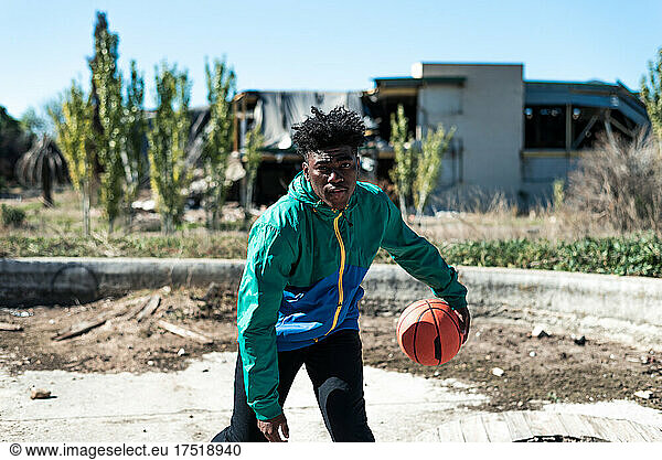 Black boy bouncing a basketball. Building in ruins.