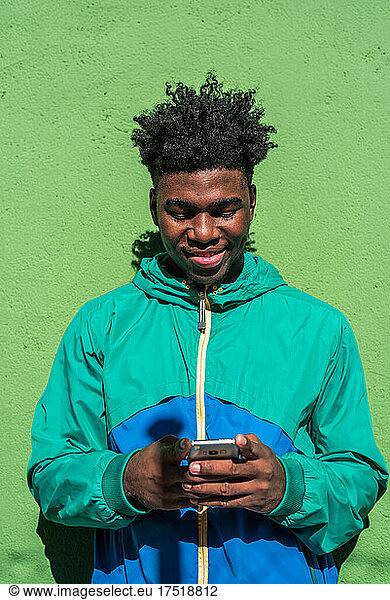 Black boy using his mobile phone. Green wall background.