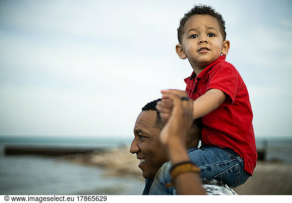 Black father gives three year old son ride on shoulders near water