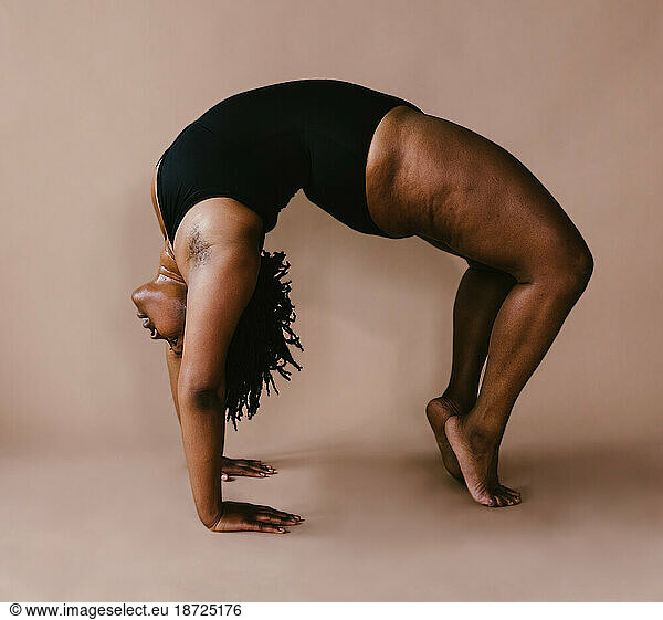 Black female dancer in backbend in front of brown backdrop
