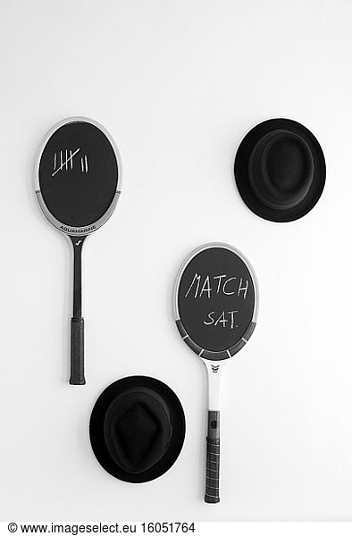 Black hats and blackboards made from tennis rackets hanging on white wall