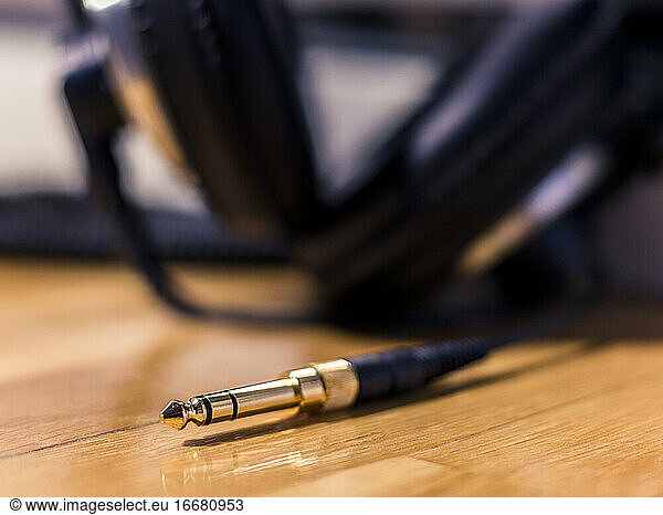 Black Hi-Fi headphones with a gold input jack on a wooden floor