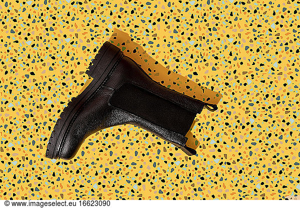 Black leather boot on yellow terrazzo pattern