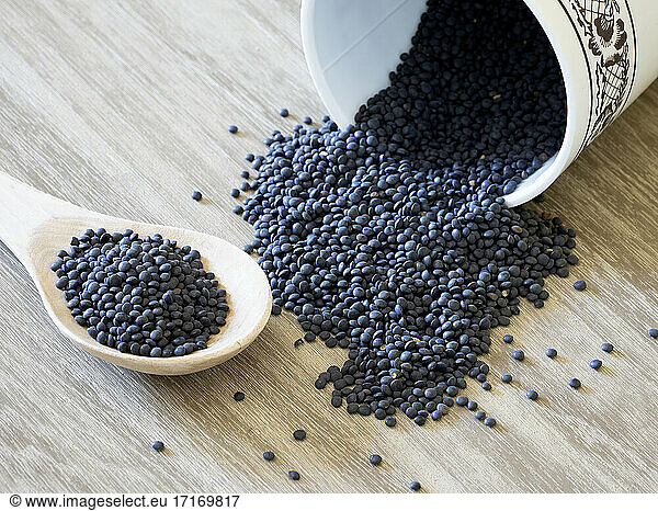 Black lentils spilling out of container lying on wooden surface