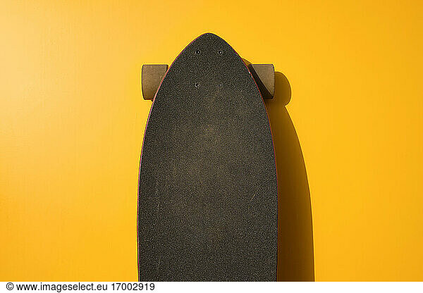 Black longboard leaning on yellow wall