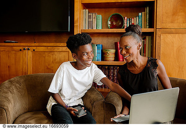 Black mom and preteen son smiling together during distance learning