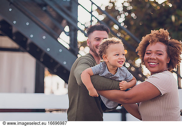 Black mom and white dad holding baby boy and playing airplane