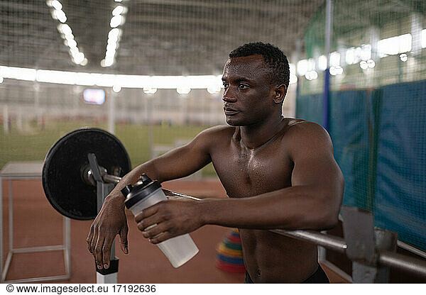 Black sportsman with water resting near barbell