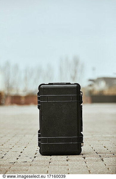 Black suitcase on footpath against clear sky