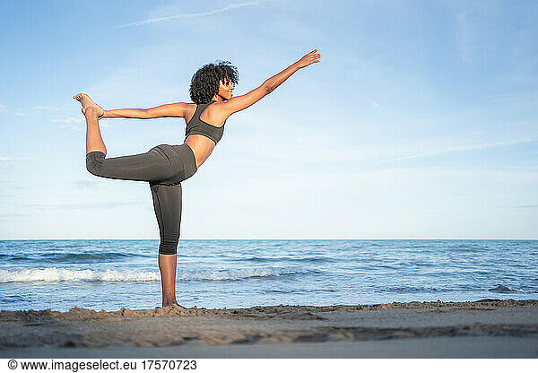 black woman smile doing yoga posture by the sea