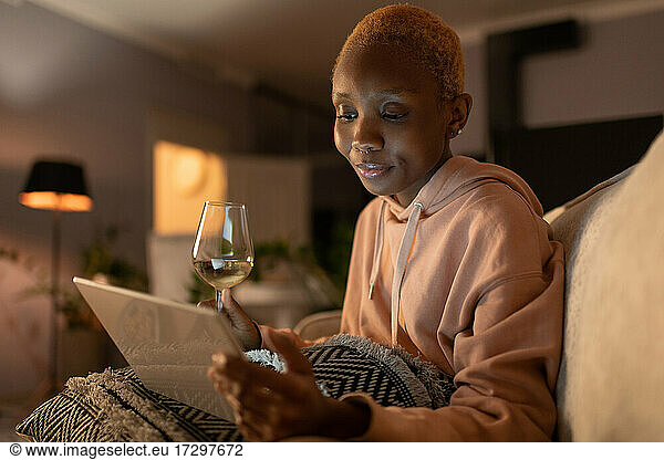 Black woman with wine and tablet resting at home
