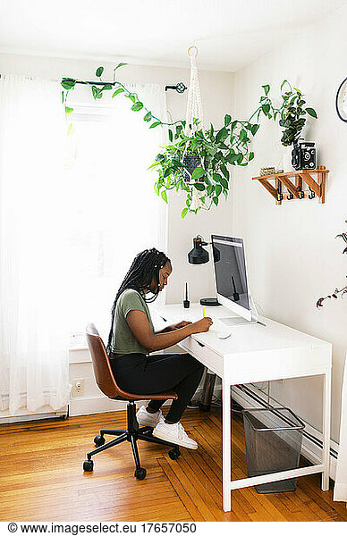 black young woman taking notes at desk and working on computer