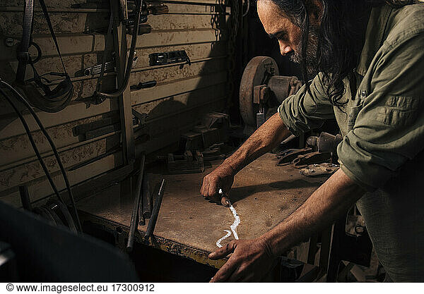 Blacksmith drawing a design for making a pair of scissors.