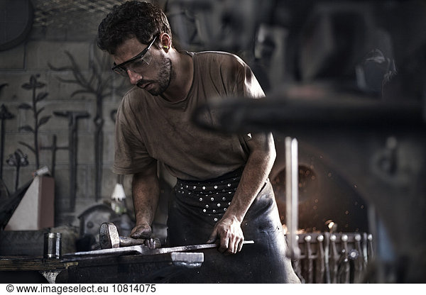 Blacksmith hammering iron at anvil in forge