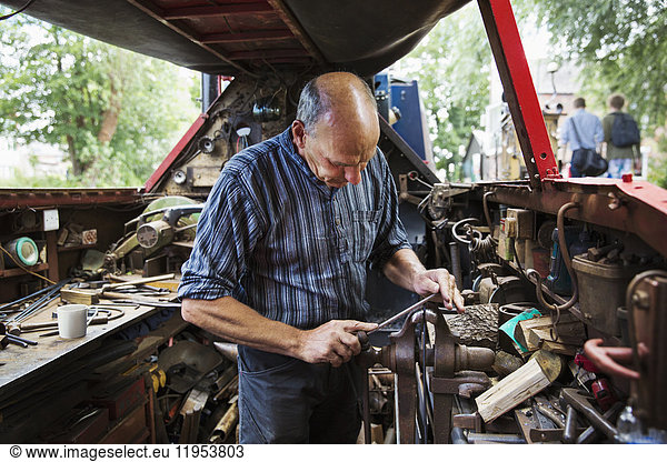 Blacksmith standing in his workshop  a floating forge on a narrowboat barge  working on a metal object  using a file.